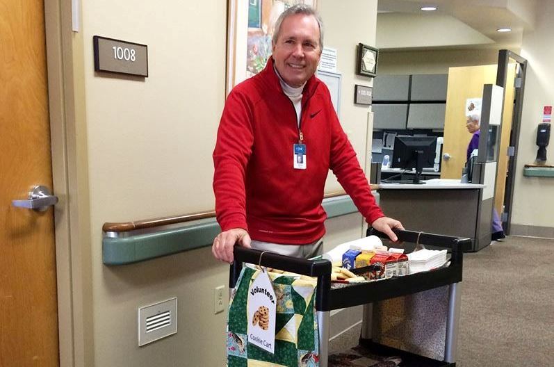 A TMC volunteer wheels a decorated cart with cookies and cartons of milk to hospice patients.